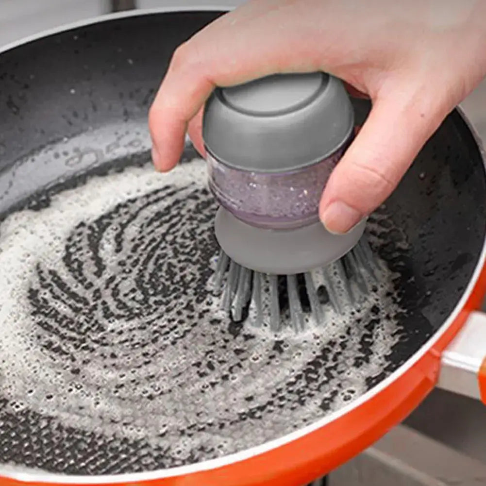 Hand using multifunctional cleaning brush soap dispenser on a frying pan for easy washing.